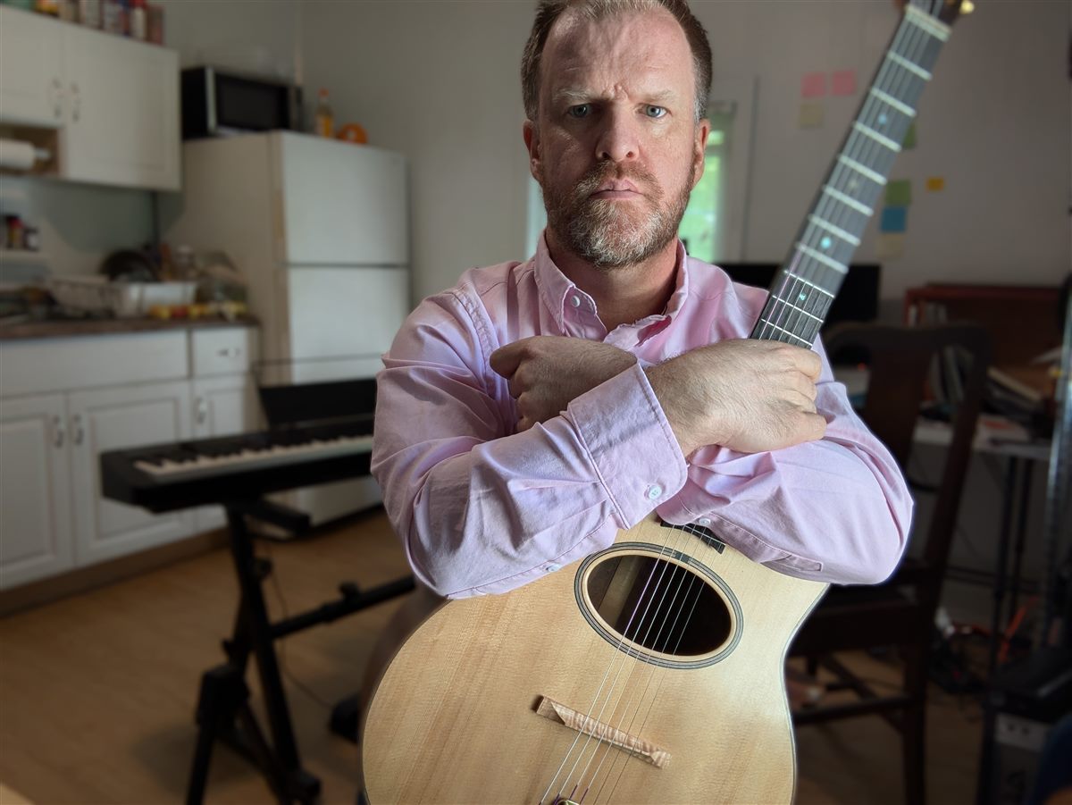 Paul McEvoy holding a guitar neck in his workshop.