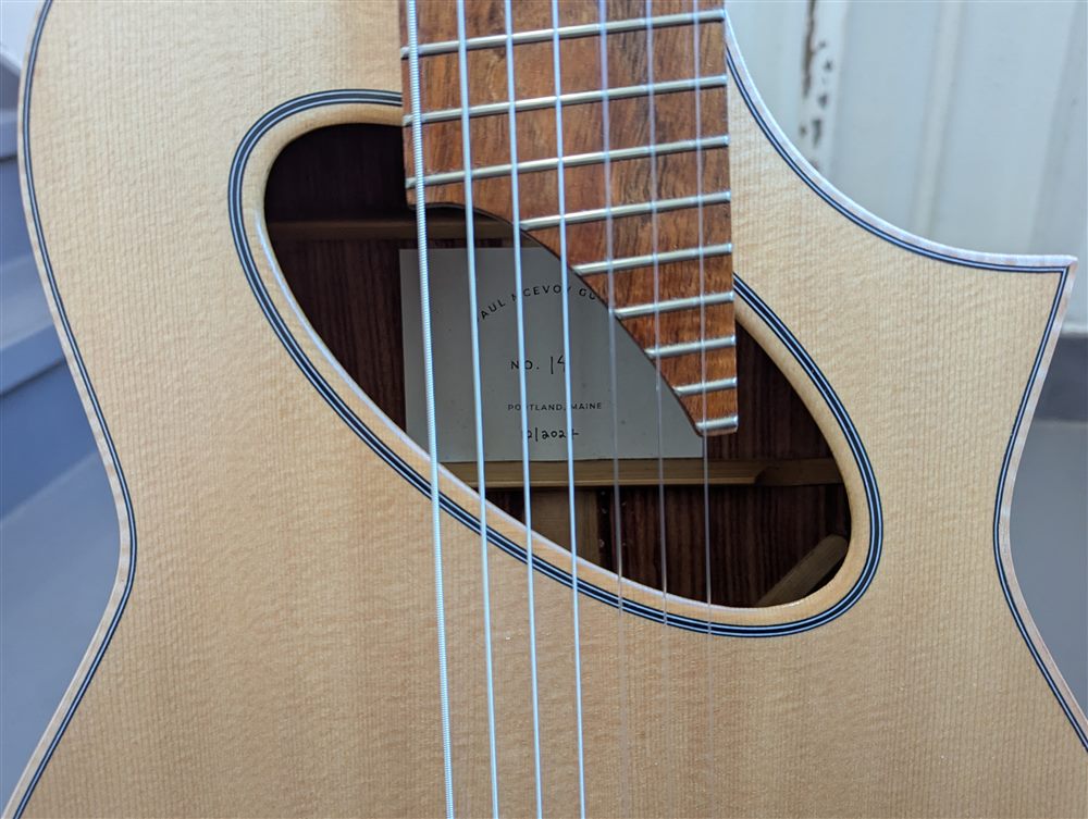 Interior label of Paul McEvoy Guitars visible through the soundhole of a handbuilt 7-string multiscale guitar.